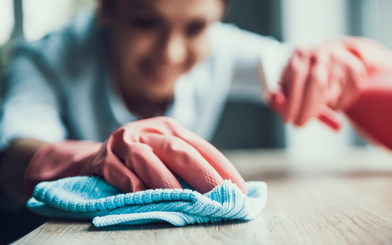 A table top being wiped down by hand with a cloth and spray