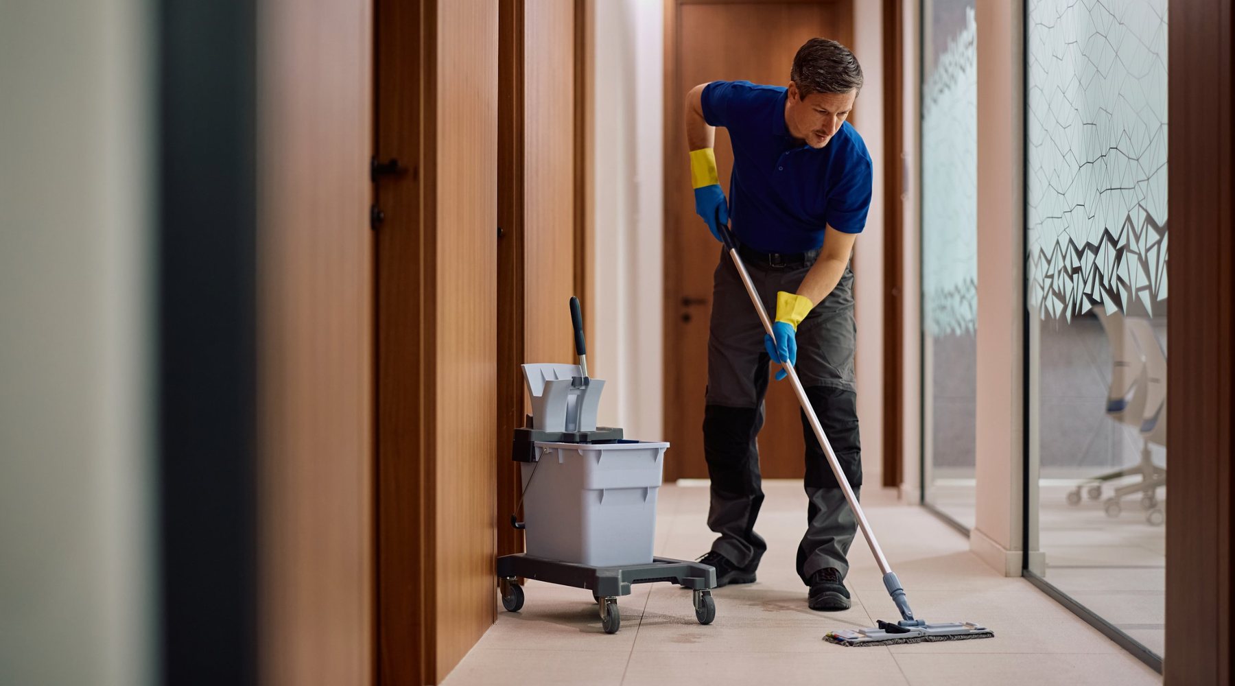 A Heralding cleaner mopping the floor of an office corridor